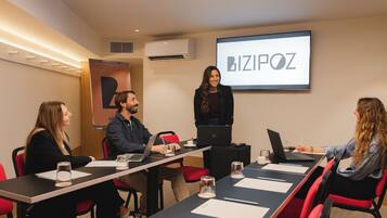 A conference room with a long table, red chairs, laptops, and a projector screen displaying "BIZPOZ".