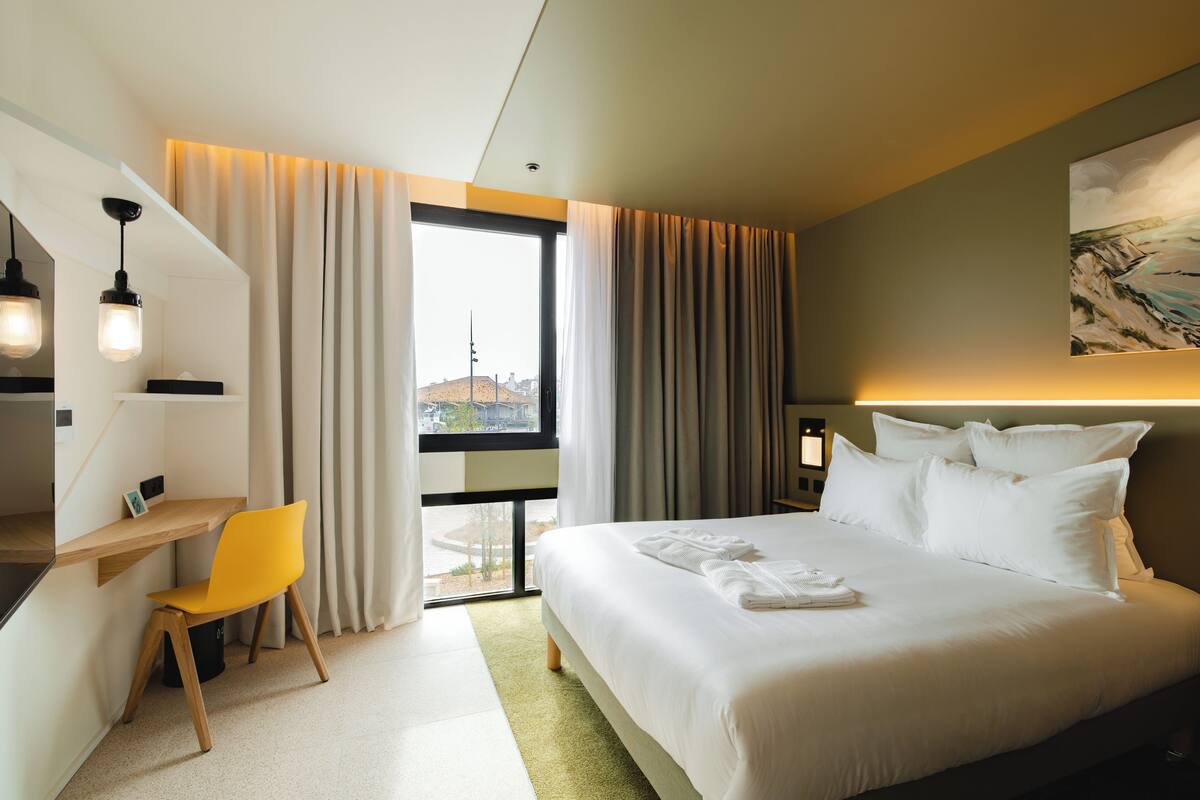 Habitación de hotel con cama, escritorio, silla y ventana con cortinas.