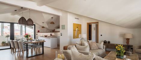 A spacious living area with a dining table, sofas, and a kitchen in the background.