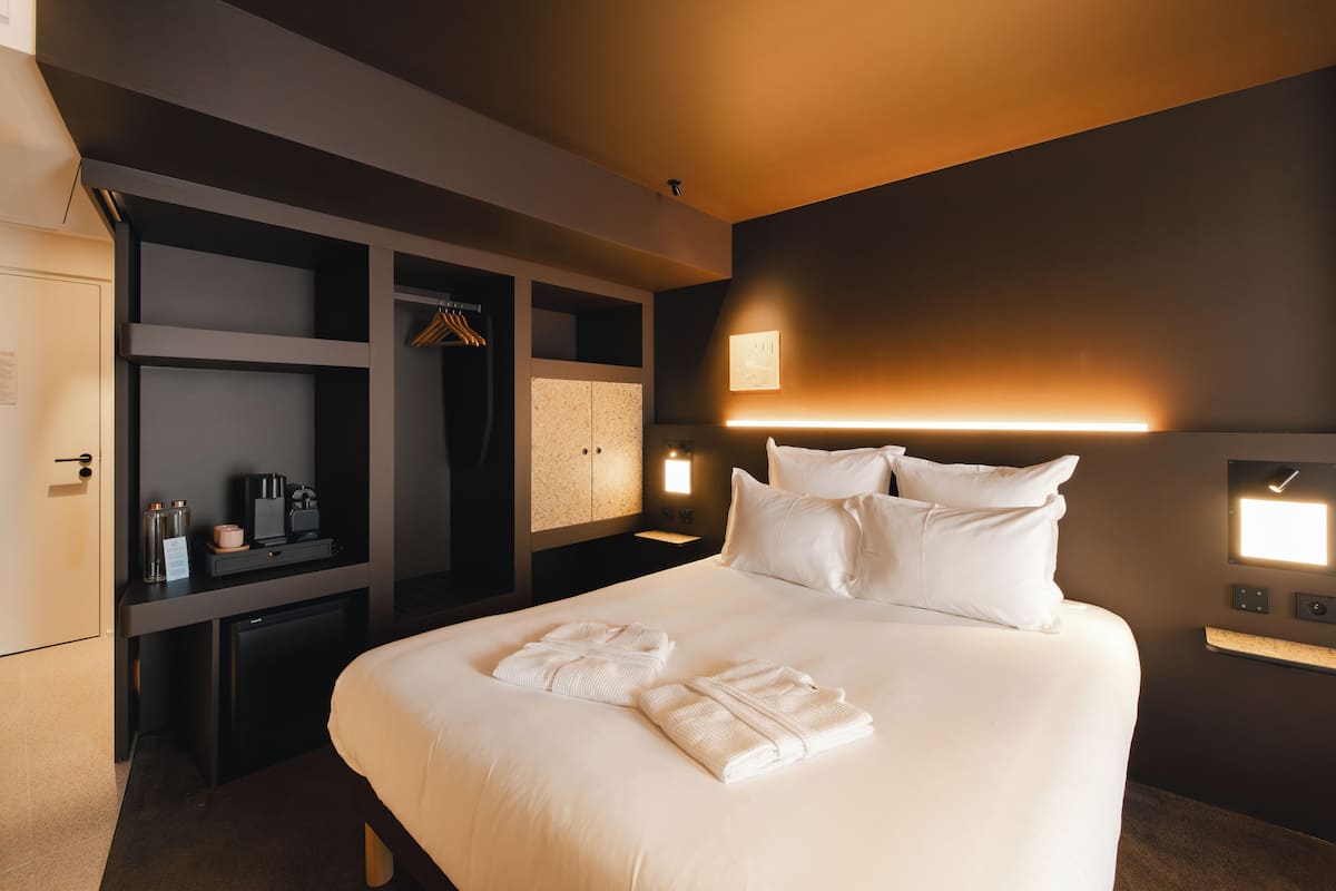 Una habitación de hotel con cama, armario, escritorio y mesita de noche.