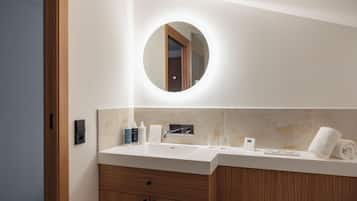 Un baño moderno con un espejo redondo, un lavabo blanco, armarios de madera y una toalla en la encimera.
