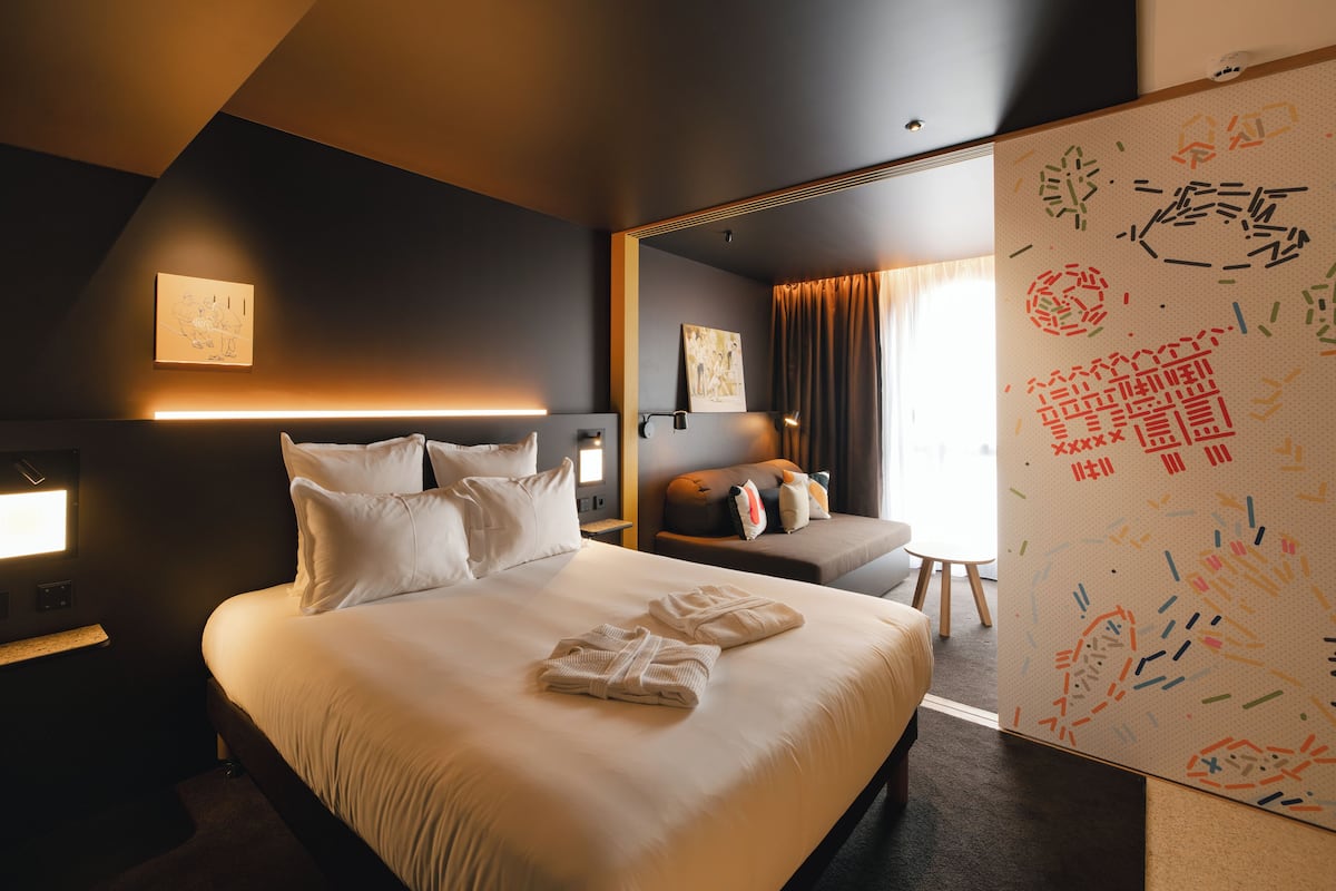 Una habitación de hotel moderna con una cama grande, zona de estar y vistas a la ciudad.