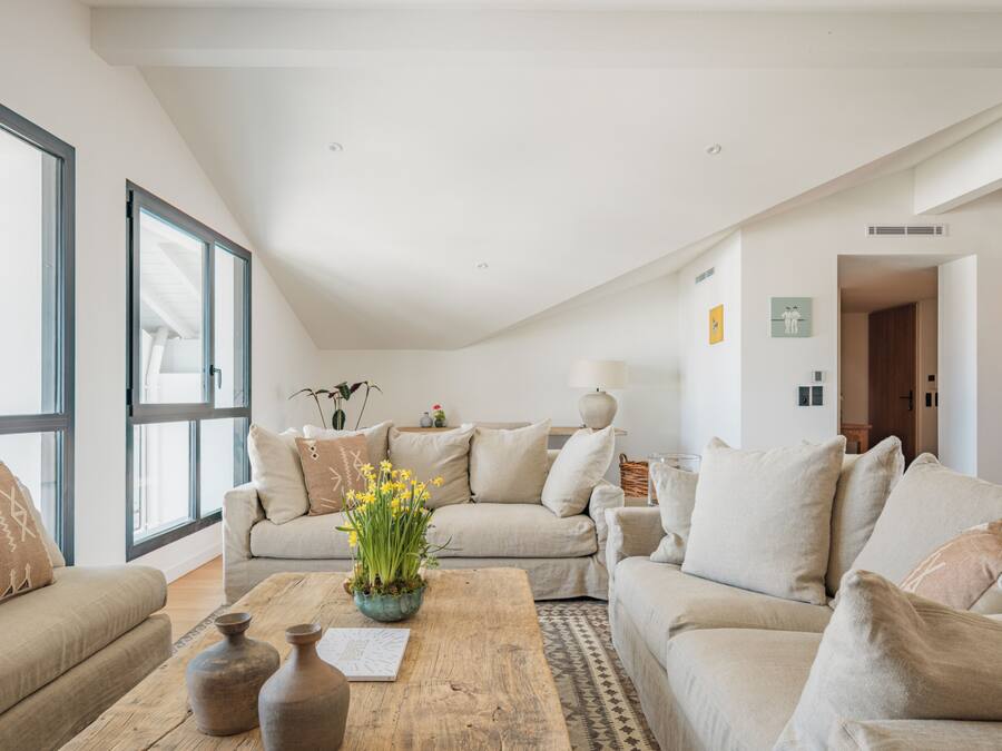 A modern living room with a wooden coffee table, beige sofas, and large windows.