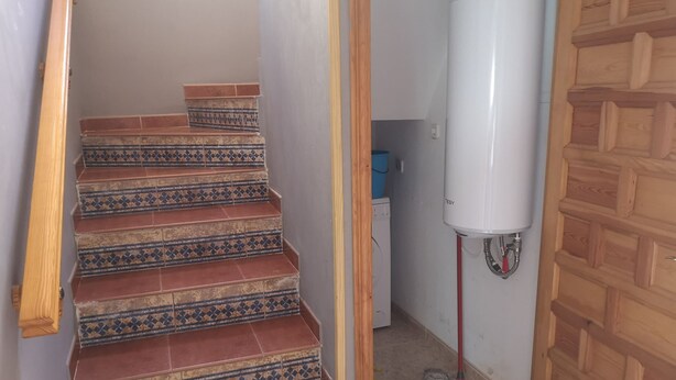 Eine Treppe mit gemusterten Fliesen führt zu einem Raum, in dem ein weißes Warmwassergerät und ein Wischmopp stehen.