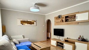 Un salon moderne comprenant un canapé, une table basse, un téléviseur, des étagères en bois et un ventilateur de plafond.