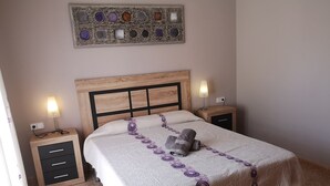 Un lit bien fait, recouvert d’une couvre-lit à motifs, deux tables de chevet avec des lampes, une œuvre d’art murale au-dessus du lit et une tête de lit en bois.