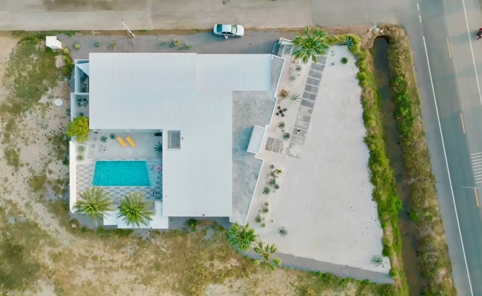 Vue aérienne d’un bâtiment moderne doté d’une piscine, d’un espace de détente extérieur et d’un parking.