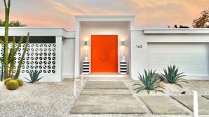 A modern house with a red door, white garage, and a number 142 on the garage door.