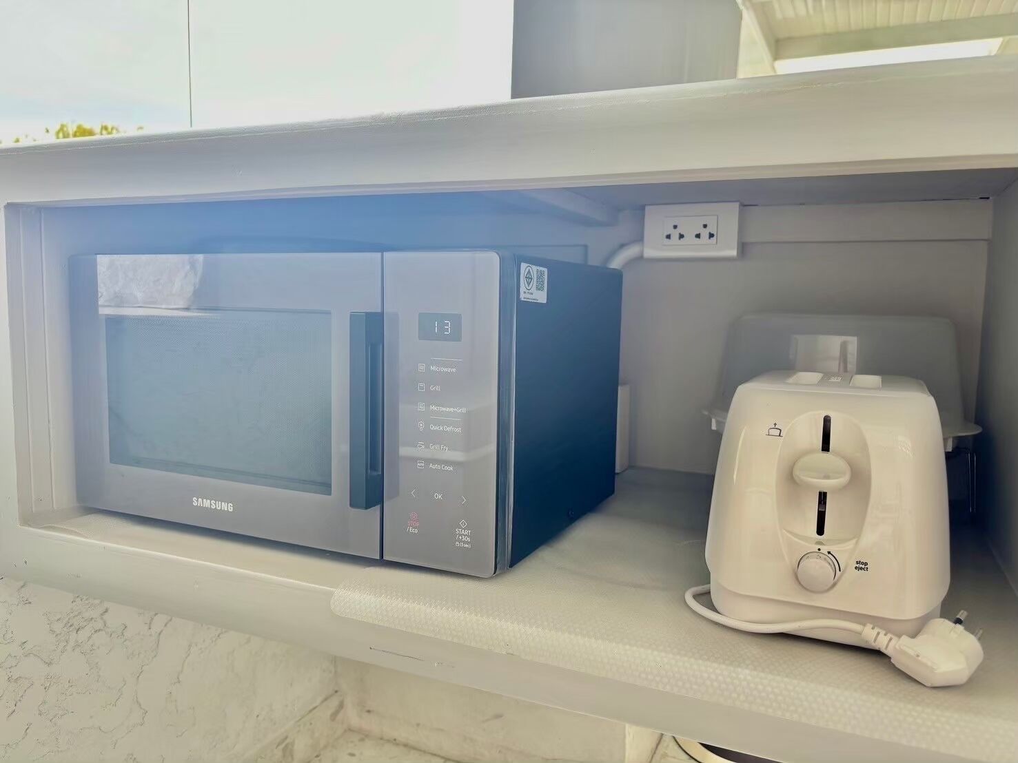 Un four à micro-ondes doté d’un écran numérique et un grille-pain, tous deux posés sur un plan de travail blanc.