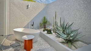 A modern bathroom with a freestanding bathtub, a small table, and a variety of plants including a large agave.