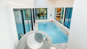 Una piscina interior moderna con paredes de vidrio transparente, techo de madera y vistas al exterior.