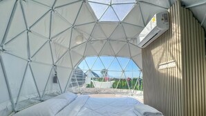Una habitación con forma de cúpula, con una cama, un ventanal y un equipo de aire acondicionado.