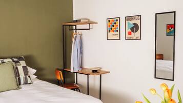 Habitación de hotel con cama, escritorio, silla, mesita con un jarrón de tulipanes y dos cuadros en la pared.