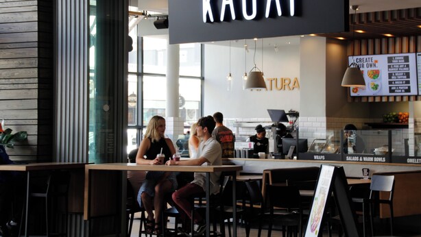 A restaurant interior with a sign reading "Kauai" and a menu board displaying food options. - Fools Inn (Cape Town)