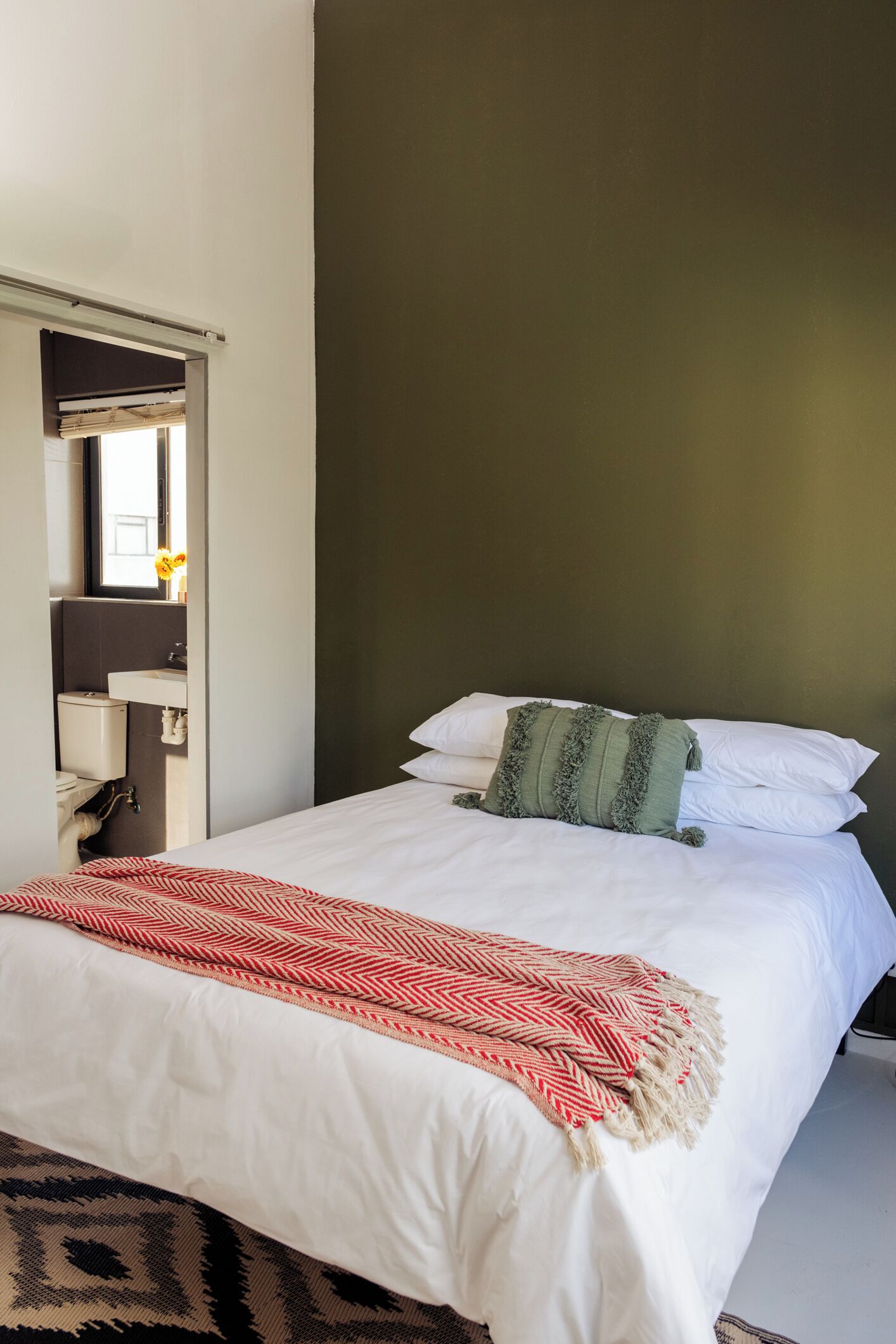 A neatly made bed with white linens and a red and white patterned throw blanket.