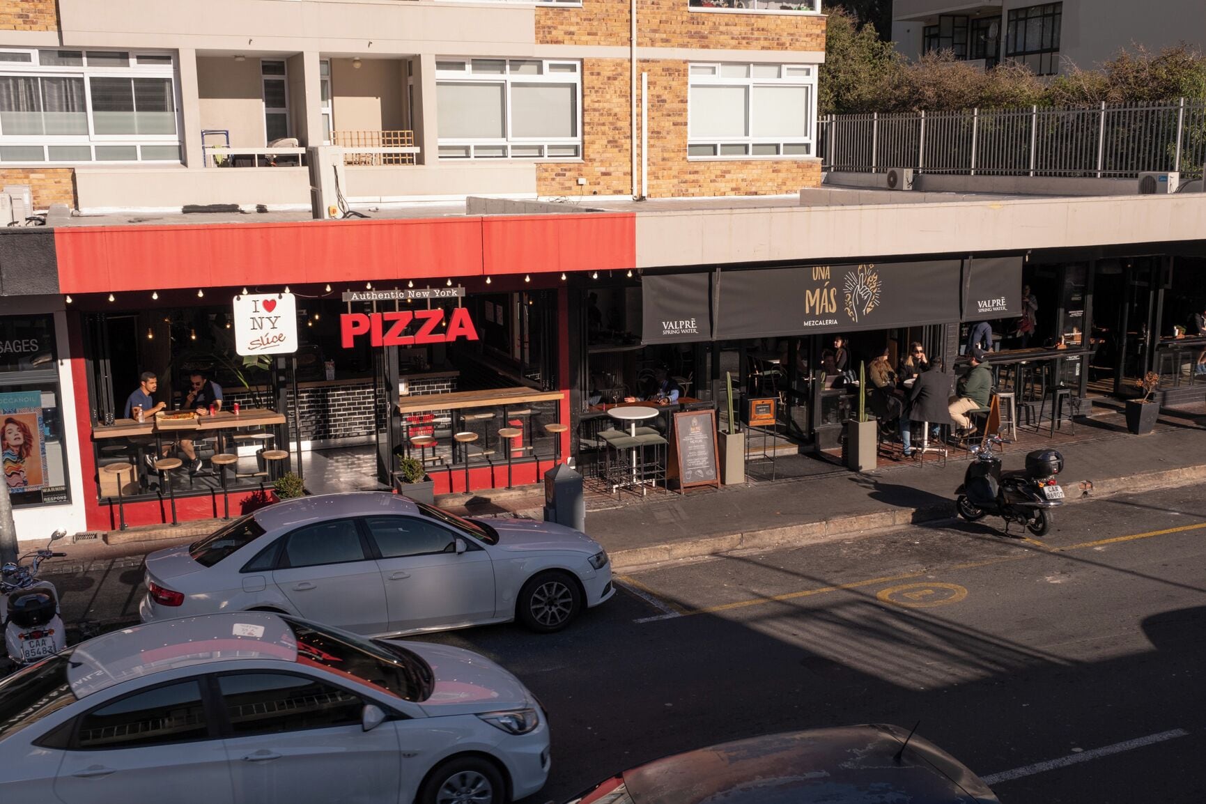 Vista da rua com um restaurante de pizza e uma padaria.