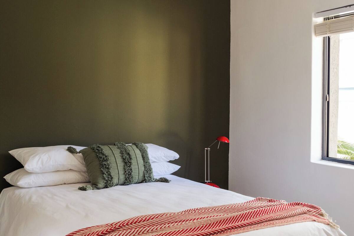 A bed with white bedding and a red and white patterned throw blanket.