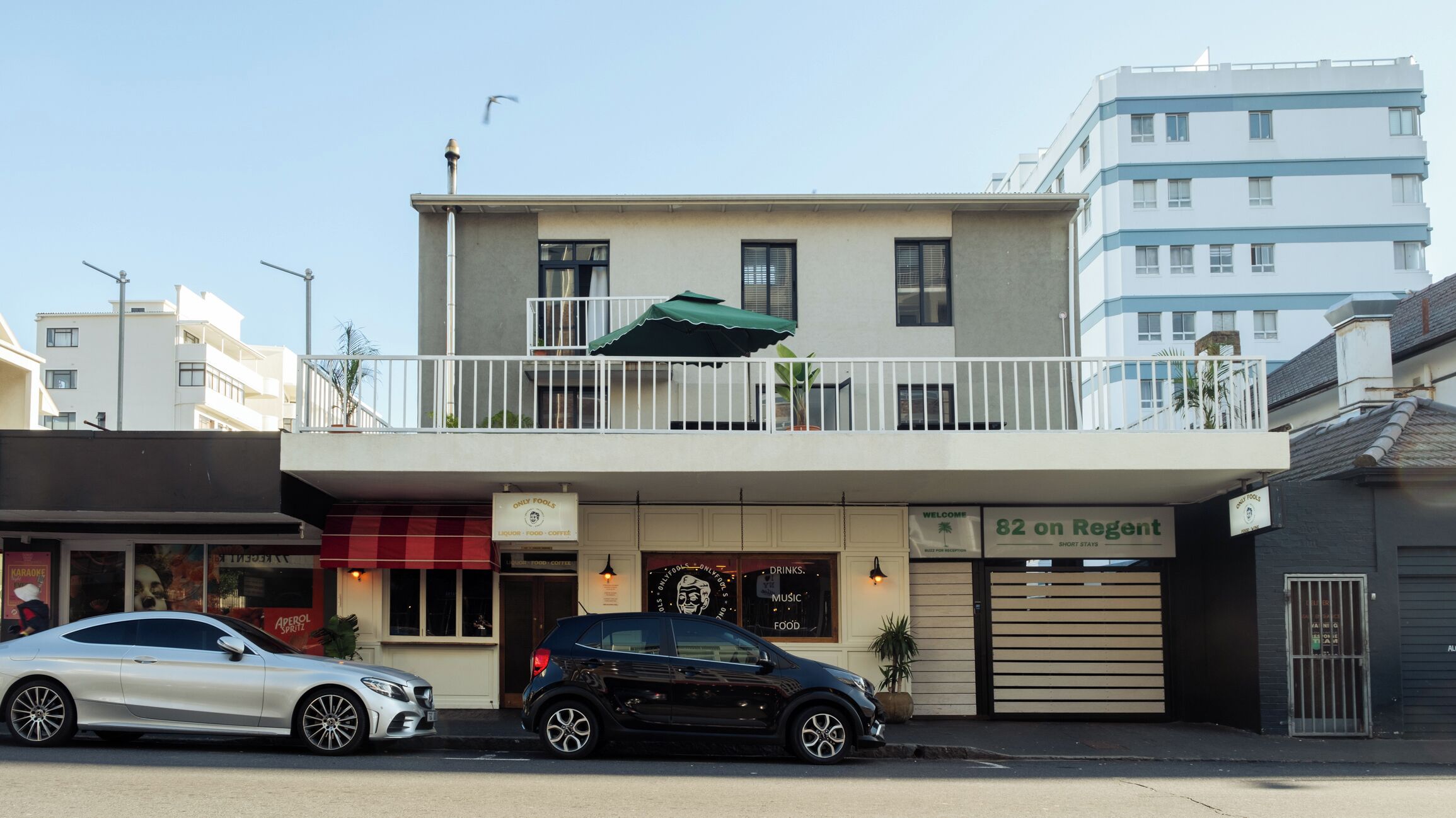 A building with a balcony, a sign for '82 on Regent', and two parked cars.