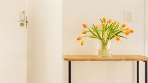 A room with a white door, a wooden table with a clear glass vase containing orange tulips, and a light switch on the wall. - Fools Inn (Cape Town)