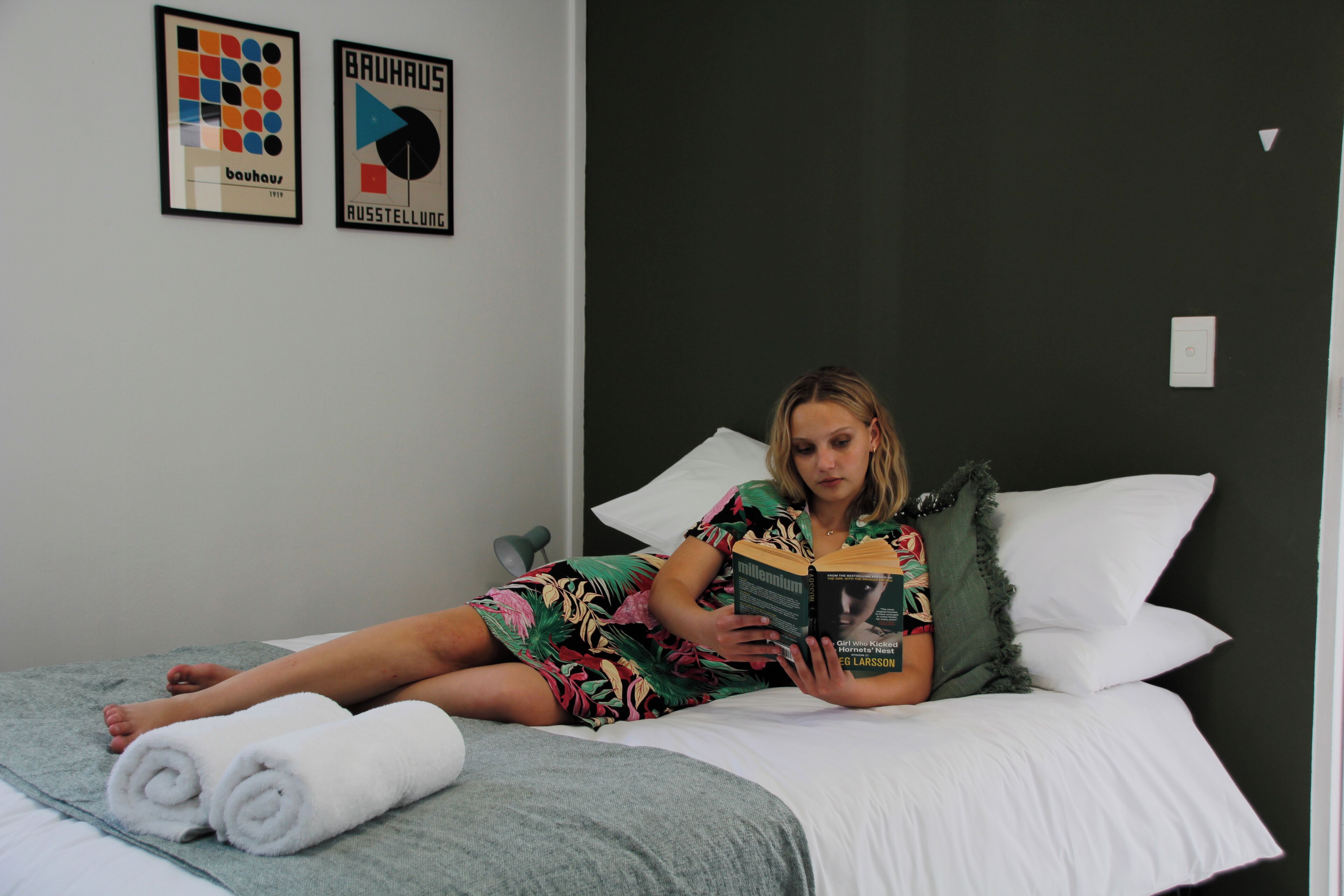 Een persoon ligt in bed met een boek, een kussen en opgerolde handdoeken.