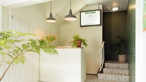 A reception desk with a 'WELCOME' sign, a potted plant, and patterned stairs leading to a dark staircase. - Fools Inn (Cape Town)