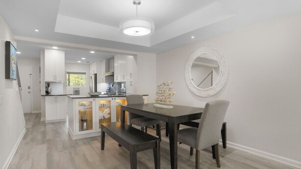 Une cuisine moderne avec des meubles blancs, une table à manger avec deux chaises et un miroir décoratif au mur.