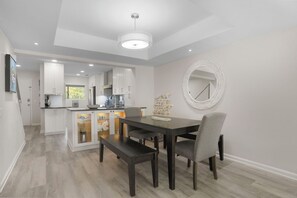 A modern kitchen with white cabinets, a dining table with two chairs, and a decorative mirror on the wall. - Courtside 119 - Forest Beach Townhome (Hilton Head Island)