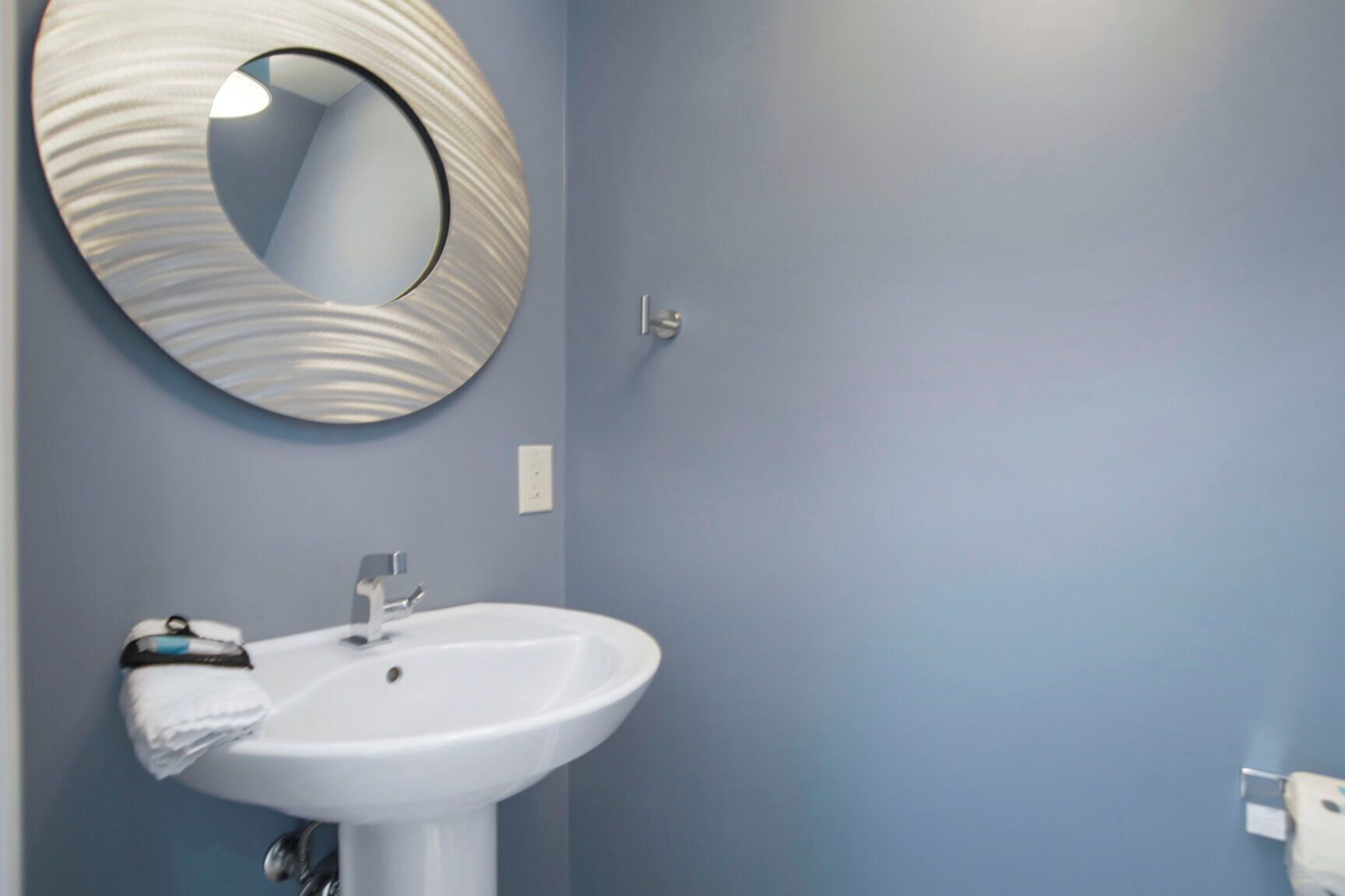 Une salle de bain avec un lavabo blanc, une serviette et un miroir rond accroché au mur.