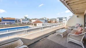 A balcony with a view of a swimming pool, white wicker furniture, and a clear sky. - 2 bedroom, 2 bath, 28th bayside with pool and tennis court! (Ocean City)