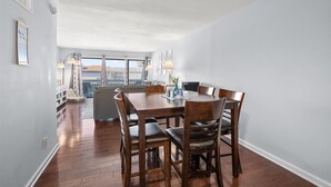 A dining area with a wooden table and chairs, a sofa, and a view through large windows. - 2 bedroom, 2 bath, 28th bayside with pool and tennis court! (Ocean City)