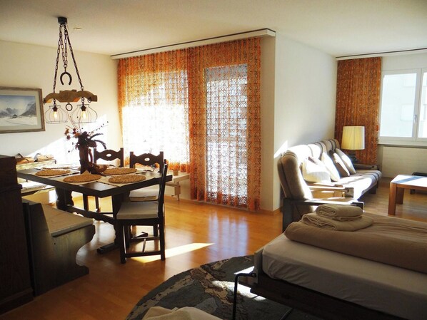 A hotel room with a dining table, chairs, a sofa, a bed, and a lamp.