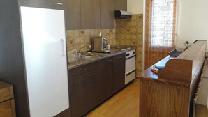 Une cuisine de taille modeste, avec des meubles de couleur sombre en bois, un réfrigérateur blanc, une cuisinière et un évier.