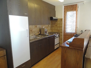 A compact kitchen with dark wooden cabinets, a white refrigerator, a stove, and a sink. - Sunnmatt Süd Wohnung 631 Appartement/Fewo 5-Bettwohnung by Interhome (Engelberg)
