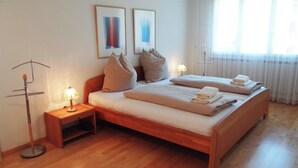 Une chambre d’hôtel avec un lit en bois, une table de chevet avec une lampe et une fenêtre ornée de rideaux légers.