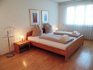 A hotel room with a wooden bed, a bedside table with a lamp, and a window with sheer curtains. - Sunnmatt Süd Wohnung 631 Appartement/Fewo 5-Bettwohnung by Interhome (Engelberg)