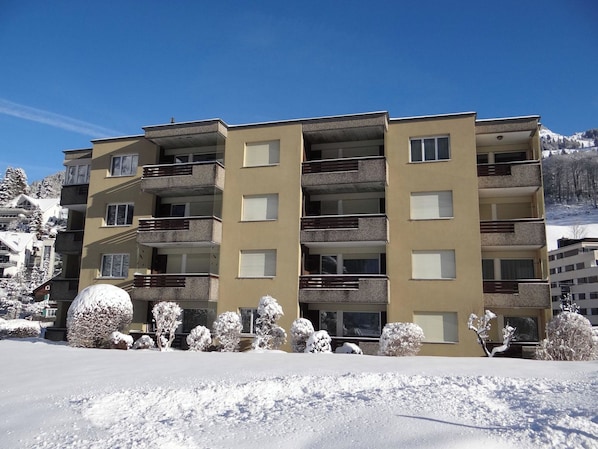 Ein mehrstöckiges Hotel mit Balkonen, eine verschneite Landschaft und ein Berg im Hintergrund.