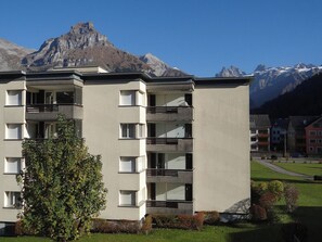 A multi-story building with balconies, set against a backdrop of mountains.