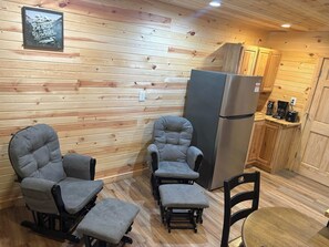 A cozy cabin interior with wooden walls, a refrigerator, and seating arrangements.