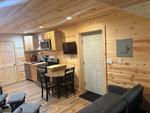 A compact kitchen with wooden cabinetry, a microwave, a stove, and a dining area with a table and chairs.
