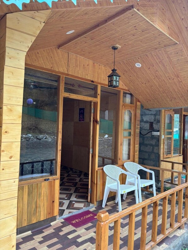 Eine Holzhütte mit überdachter Veranda, zwei weißen Plastikstühlen und einer Fußmatte.