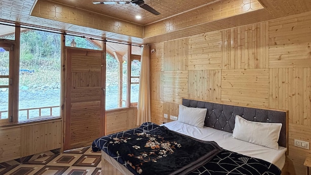 Une chambre dans une cabane en bois, avec un lit, un ventilateur de plafond et de grandes fenêtres.
