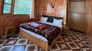Une chambre dans un chalet en bois, avec un lit, un ventilateur de plafond, une fenêtre et une armoire.