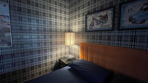 A room with a checkered wallpaper, a bed with a blue pillow, a nightstand with a lamp, and two framed pictures on the wall. - Superior Double Room (Avellino)