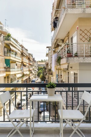 A balcony with two white chairs and a small table, overlooking a narrow street with buildings. - boat house (Thessaloniki)
