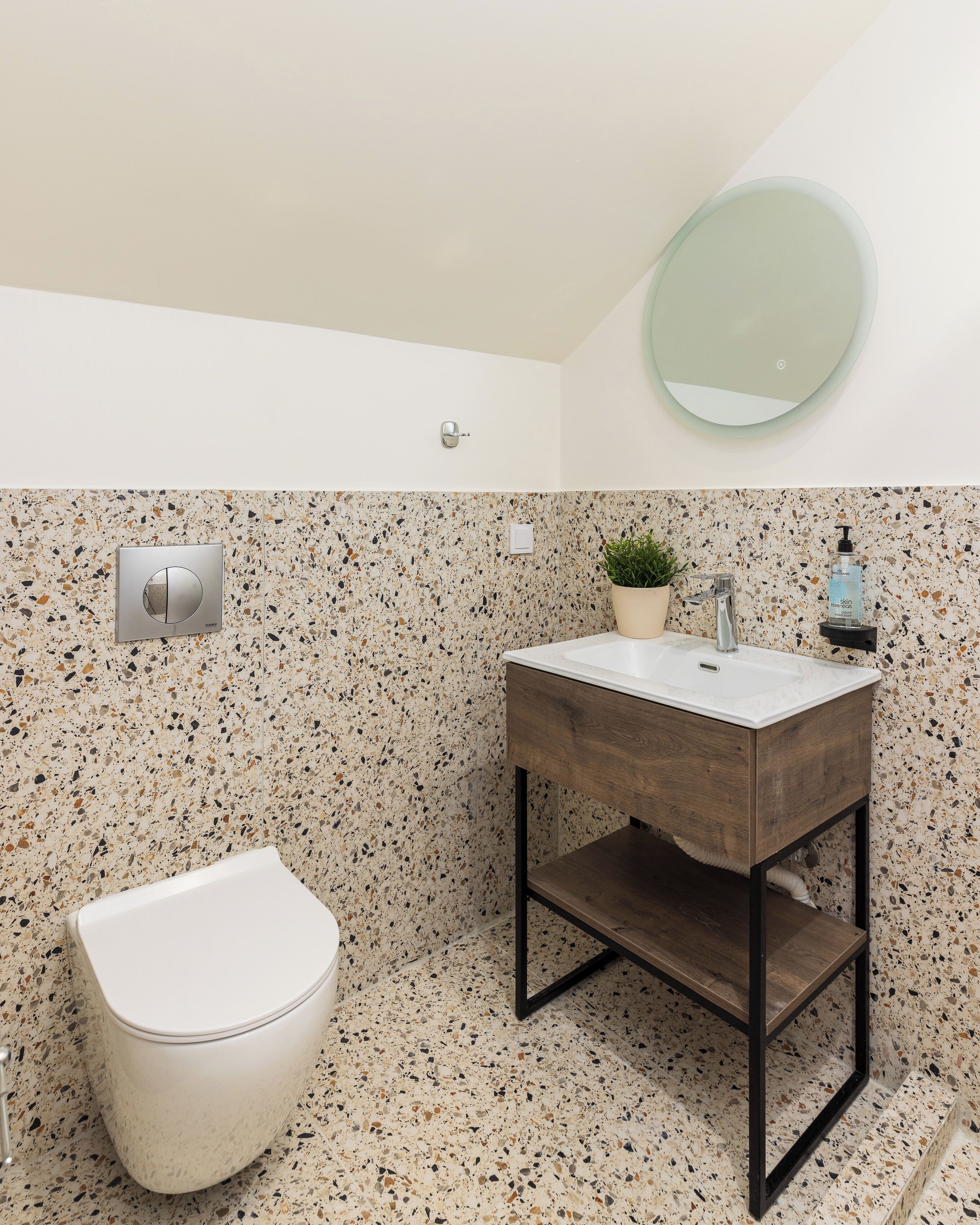 Um banheiro com vaso sanitário branco, toucador de madeira com pia, espelho e painel de azulejos com textura.