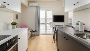 Een moderne keuken met een inbouwfornuis, een eethoek met barstoelen, een flatscreen-tv en een schuifpui naar een balkon.