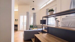 Een moderne, goed verlichte kamer met een houten bank, een grijze bank en een aan de muur bevestigde televisie.
