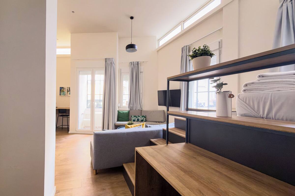 Una stanza moderna e luminosa con una panca in legno, un divano grigio e una TV a parete.