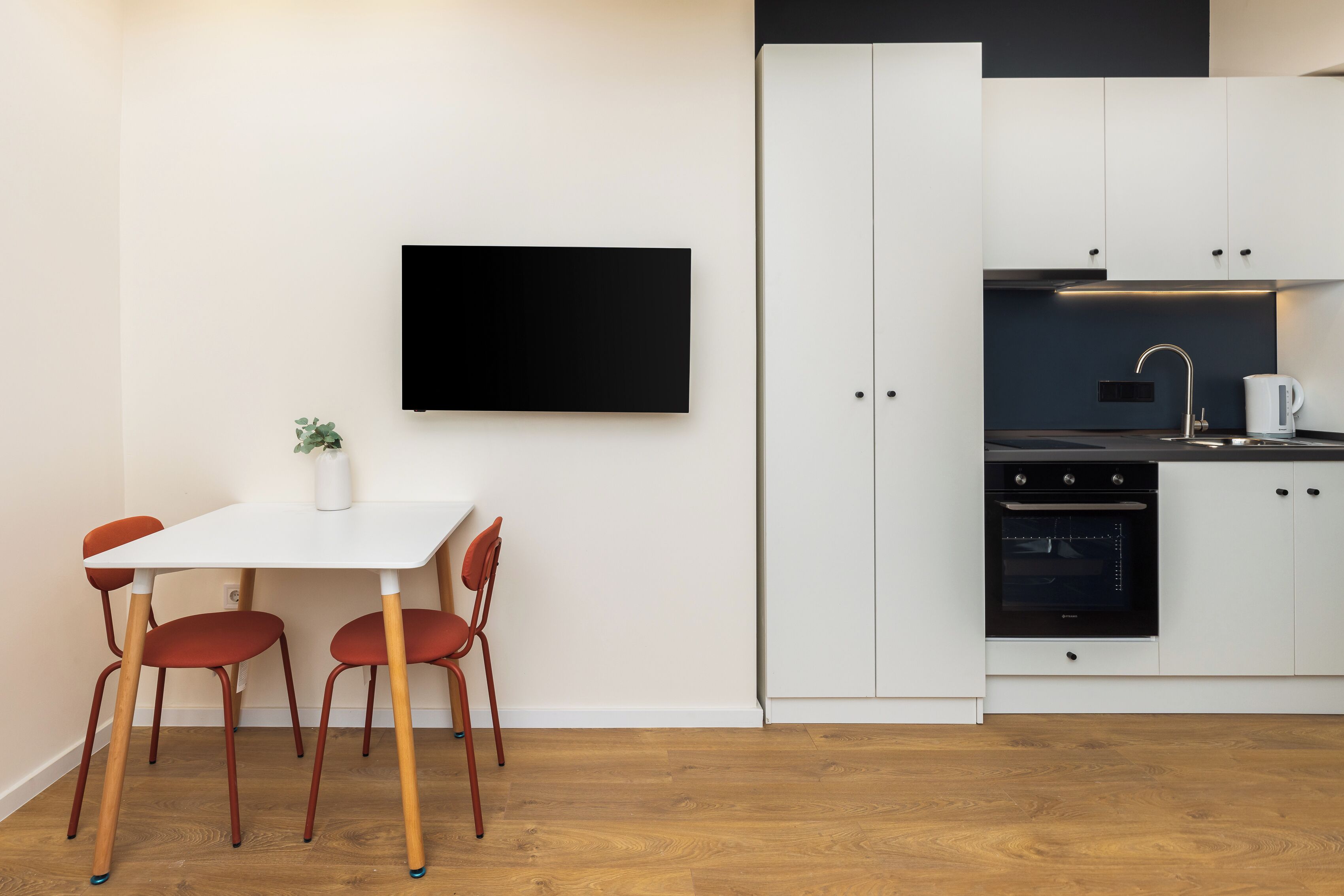 Una cocina moderna con armarios blancos, un horno negro y una mesa blanca con sillas rojas.
