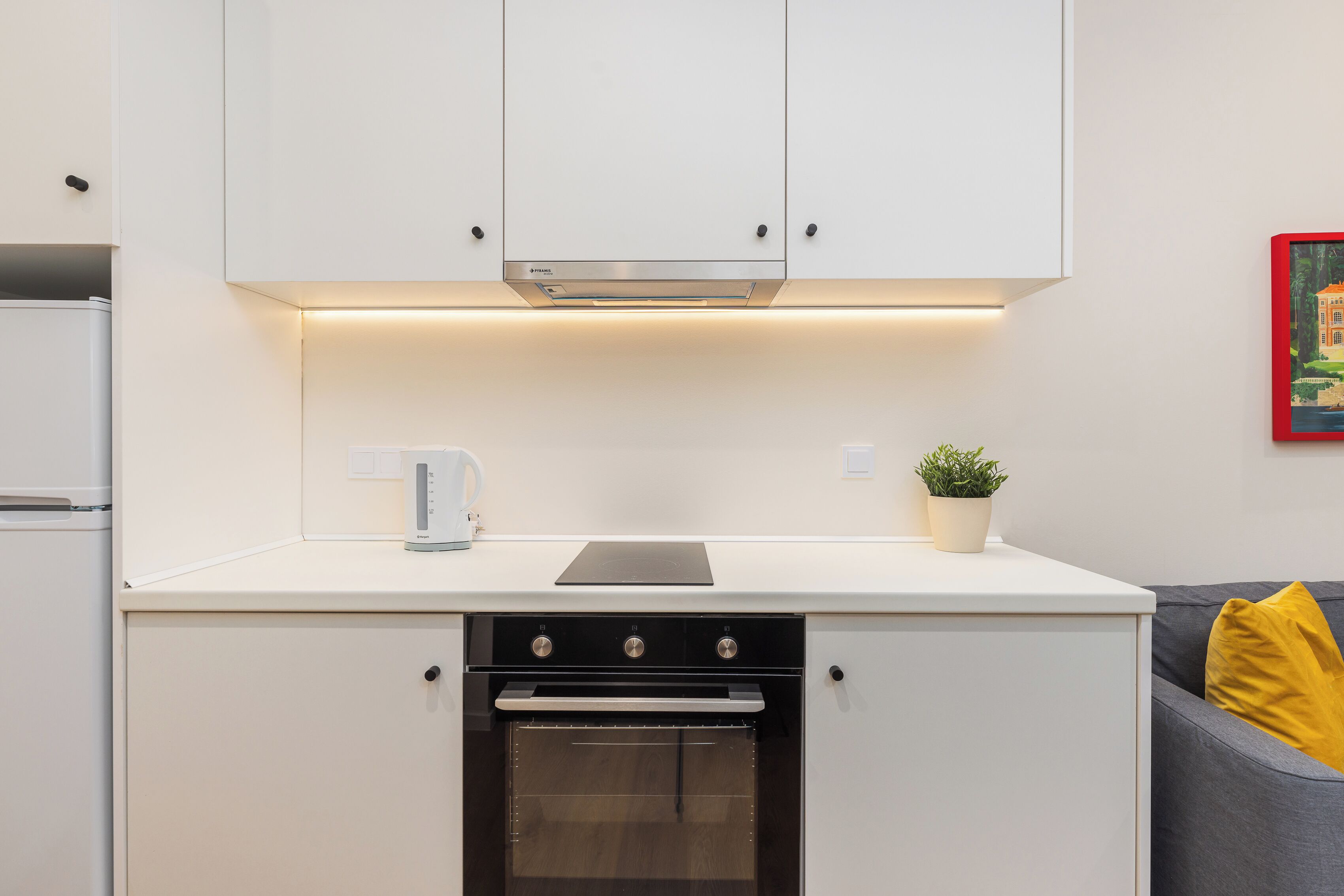 A compact kitchen with a built-in oven, a coffee maker, and a potted plant on the countertop.